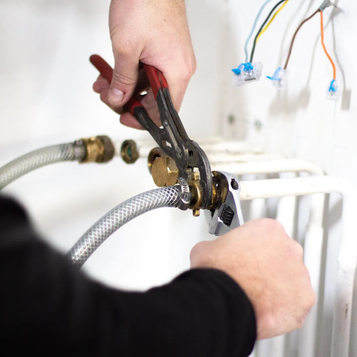Mains de technicien serrant un raccord laiton à la pince multiprise.